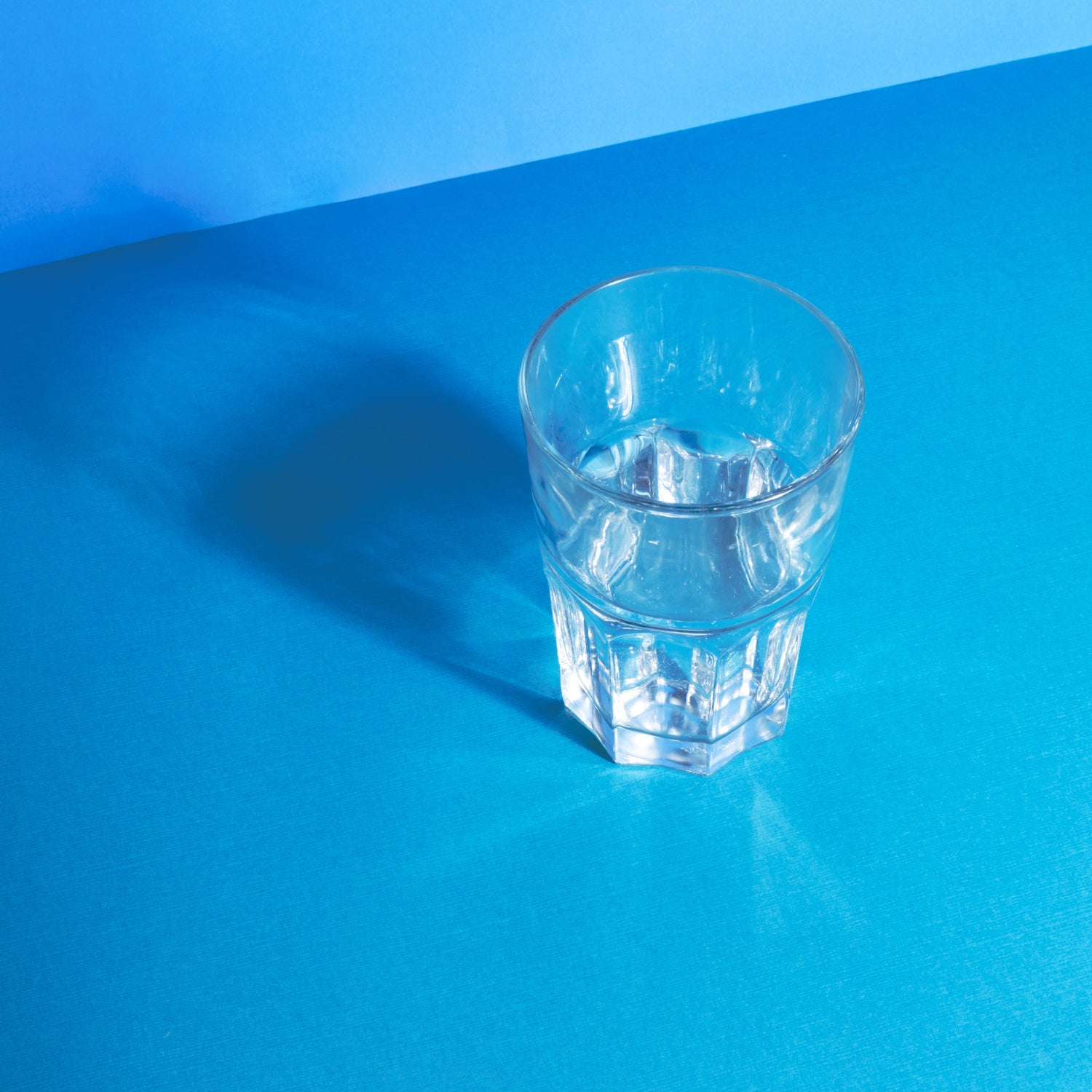 Clear water glass reflecting on a blue surface, symbolizing purity and freshness, representing Grin & Glow’s commitment to clean and effective teeth whitening services.