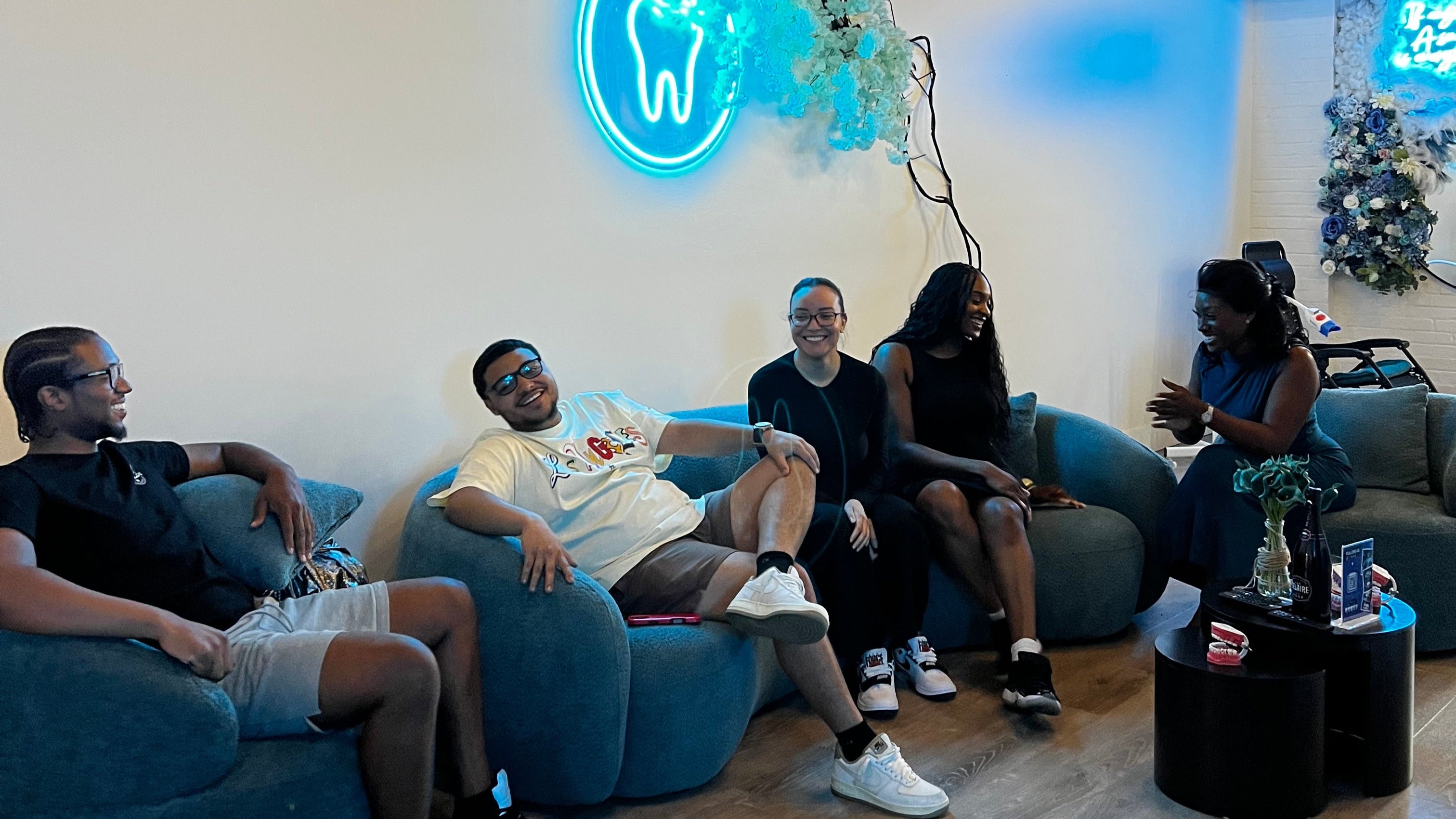 People sitting on a Grin & Glow couch with a neon sign in the center, in a modern indoor setting.