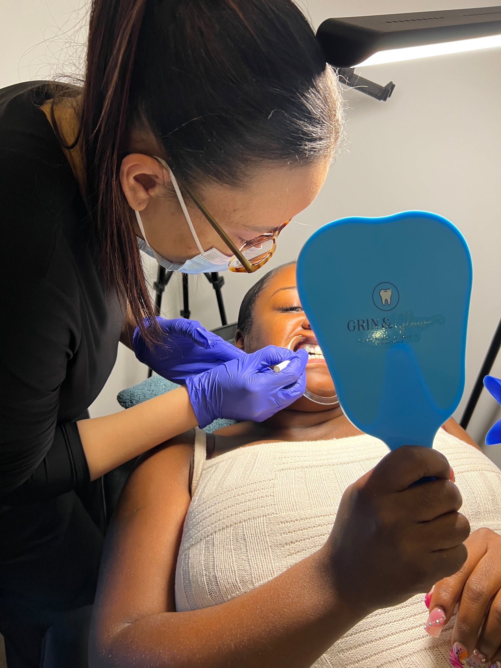 Person receiving a dental check-up with a blue dental mirror and gloved hand holding dental tools.