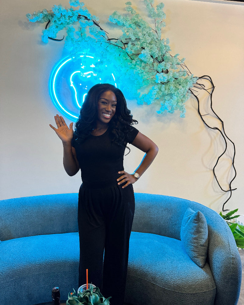 Woman in a black outfit standing in front of a blue neon sign and light blue sofa.