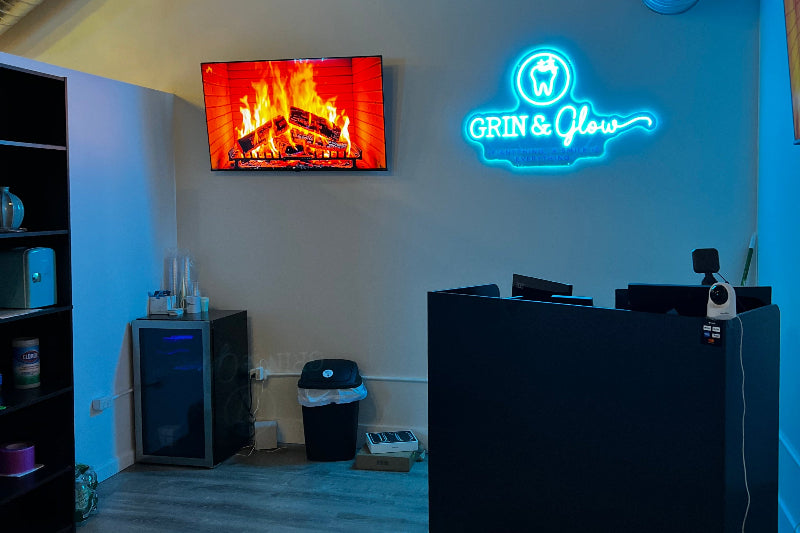 Neon sign with 'Grin & Glow' logo on a wall above a reception desk.