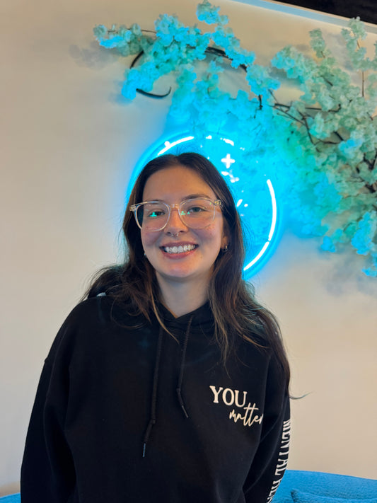 Person wearing glasses and a black hoodie with text at grin & glow, standing in front of a glowing blue circular light.