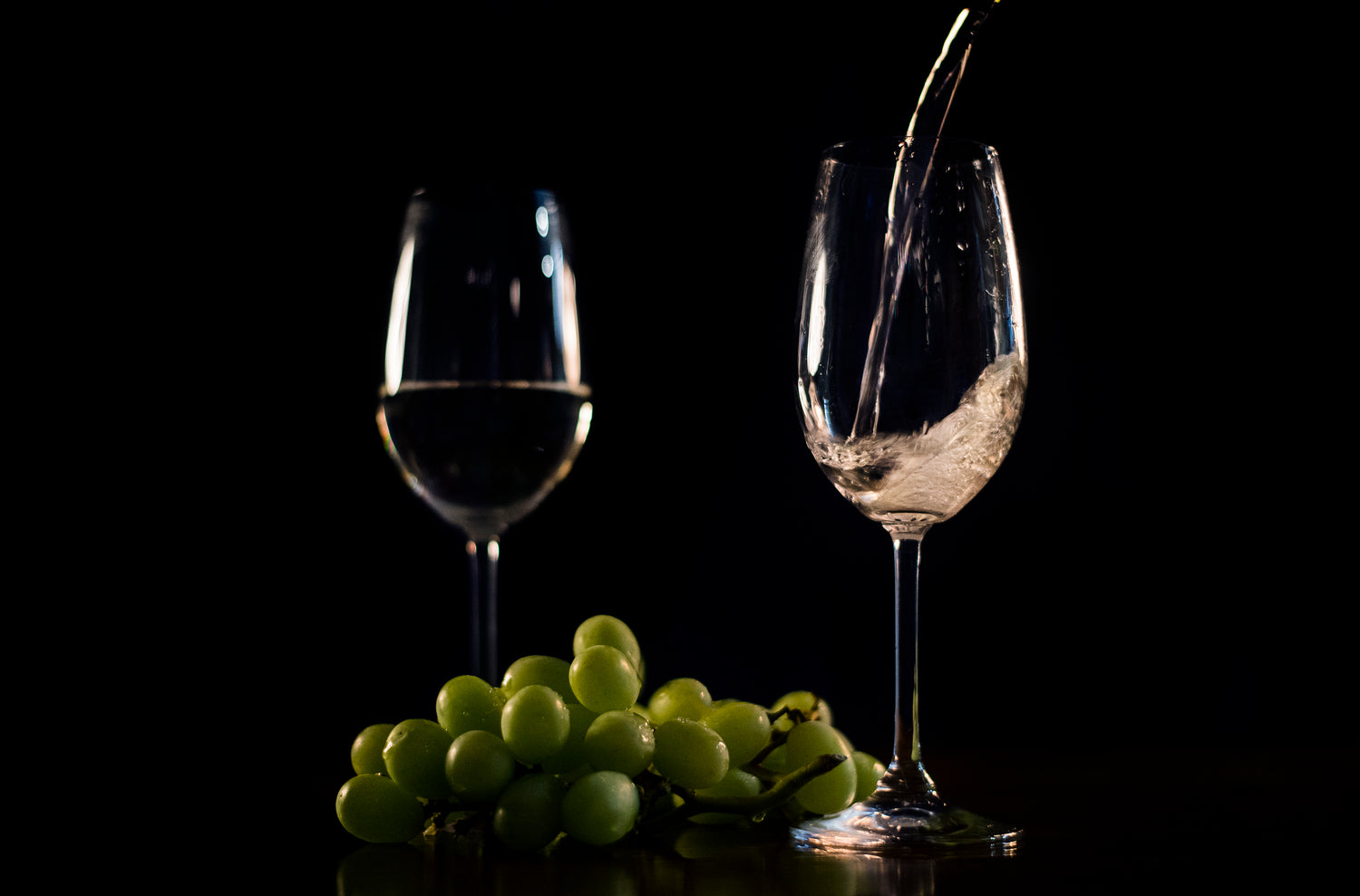 White wine pouring from a bottle with grapes beside it, symbolizing sophistication and elegance, aligning with Grin & Glow’s premium teeth whitening services