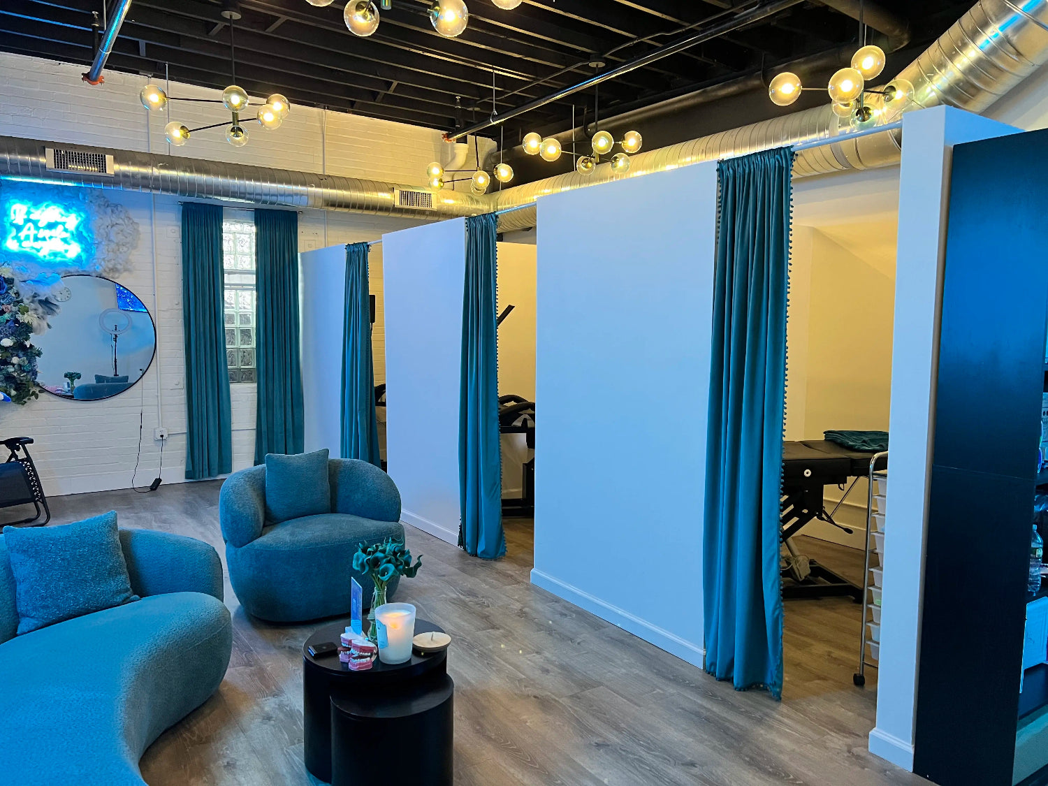 Elegant guest lounge at Grin & Glow featuring a curved teal velvet sofa, neon tooth signage with floral decor, and a relaxing, high-end atmosphere.